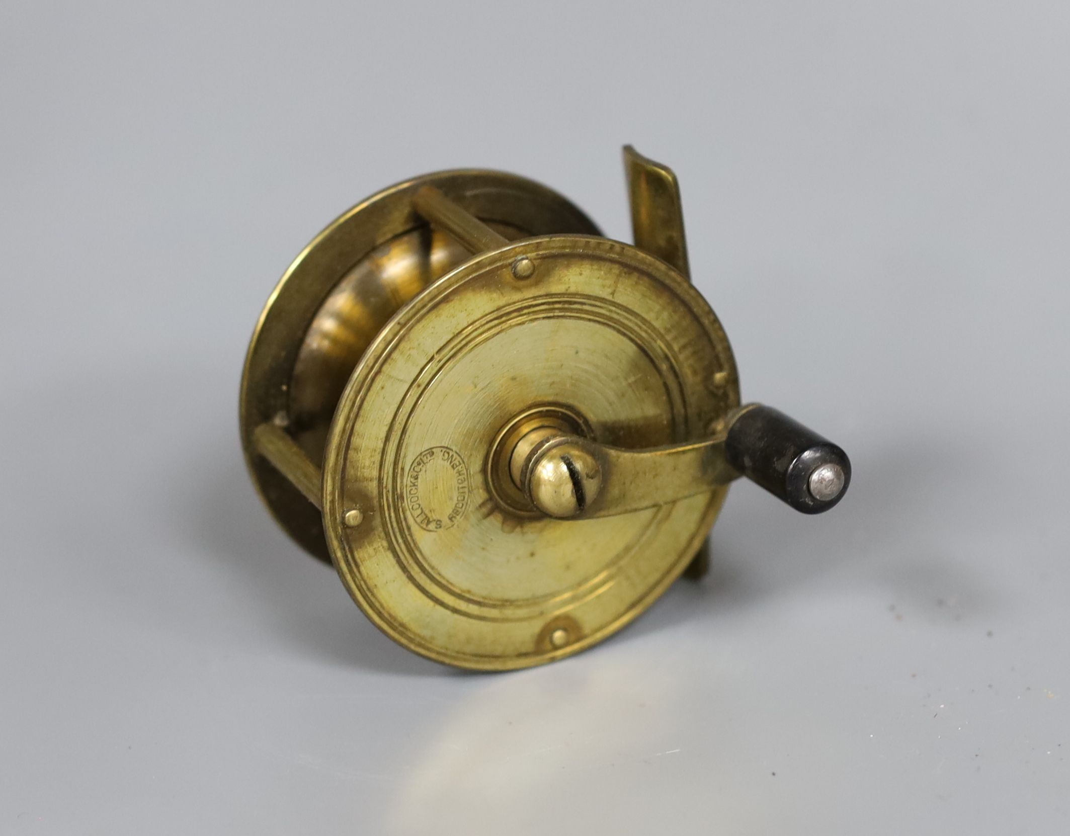 An Allcock brass fishing reel, 6cm. diam., in original box